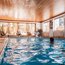 Innenpool mit Holzdecke, Hängesesseln und einer Person im Wasser