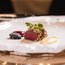 Kunstvoll angerichtetes Gericht mit rotem Fleisch, Beeren und Sauce auf weißem Teller